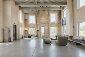 Un vestíbulo amplio con techo alto, ventanas grandes, chimenea y asientos modernos.