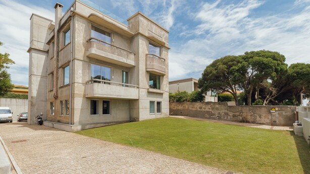 Un edificio moderno de varios pisos con fachada de piedra, camino pavimentado y césped cuidado.