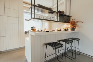 Eine moderne Küche mit weißen Schränken, einer Bar mit Hockern und einem Regal mit beschrifteten Kisten.