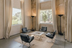 Ein Zimmer mit vier schwarzen Ledersesseln, einem zentralen Couchtisch mit Schachbrett und zwei Stehlampen.