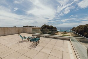 Un balcón con dos sillas y una mesa, con vista a un paisaje marino y arbolado.