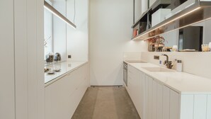 Una cocina moderna con muebles blancos, un lavamanos de acero inoxidable y un ventanal que proporciona luz natural.