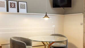 Et moderne værelse med et glasbord, to grå stole, et ophængt tv og en aircondition.