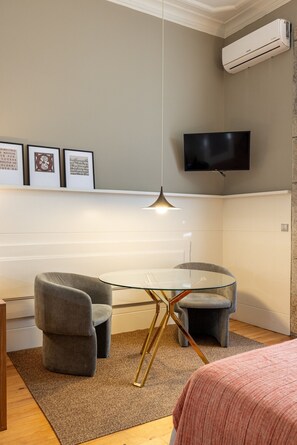 A modern room with a glass table, two grey chairs, a mounted TV, and an air conditioning unit. - Casa do Ofício - Bookseller 1 by Hosty (Porto)
