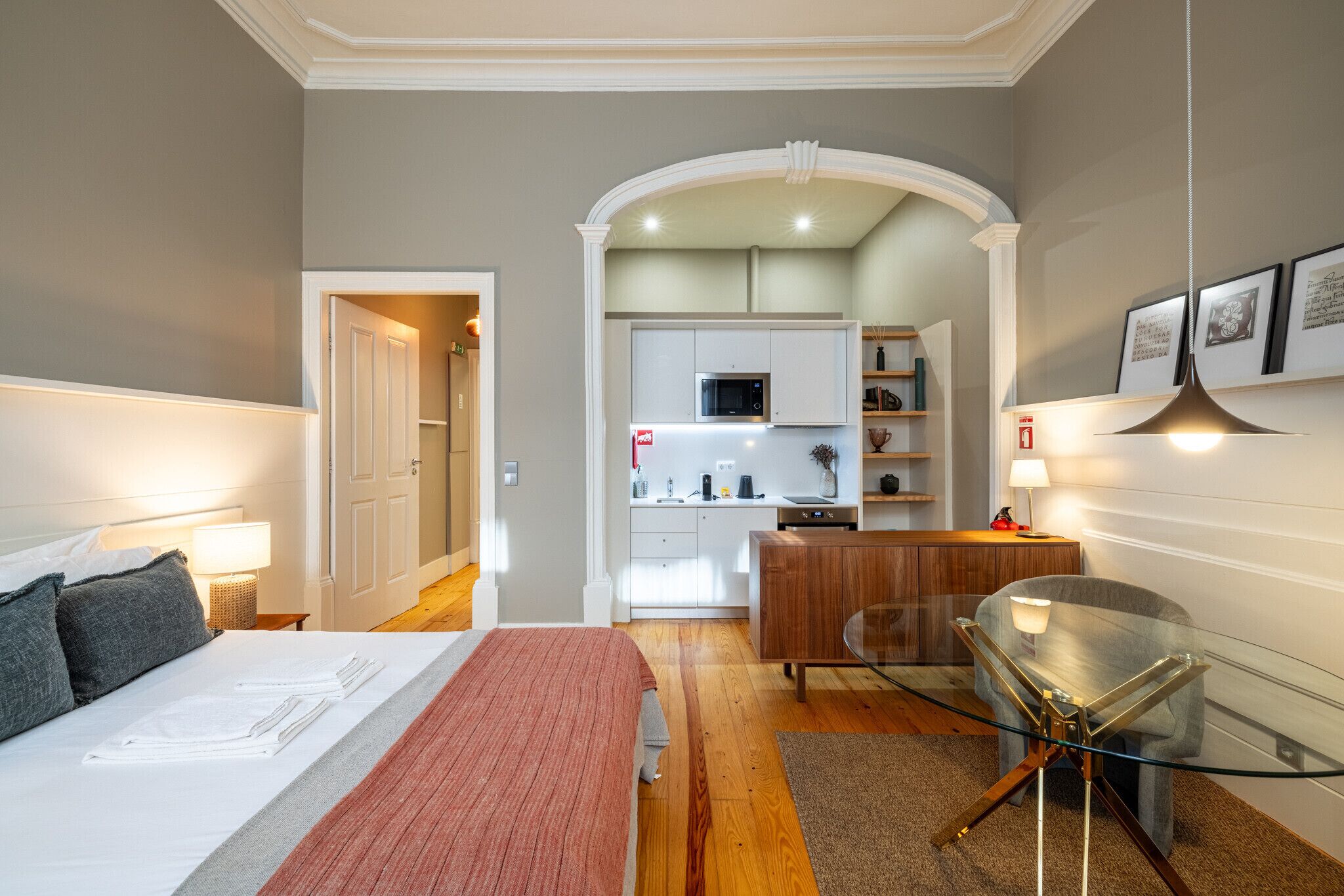 Una habitación de hotel moderna con una cama, una mesa de vidrio, una zona de cocina y un pasillo que conduce a otra habitación.