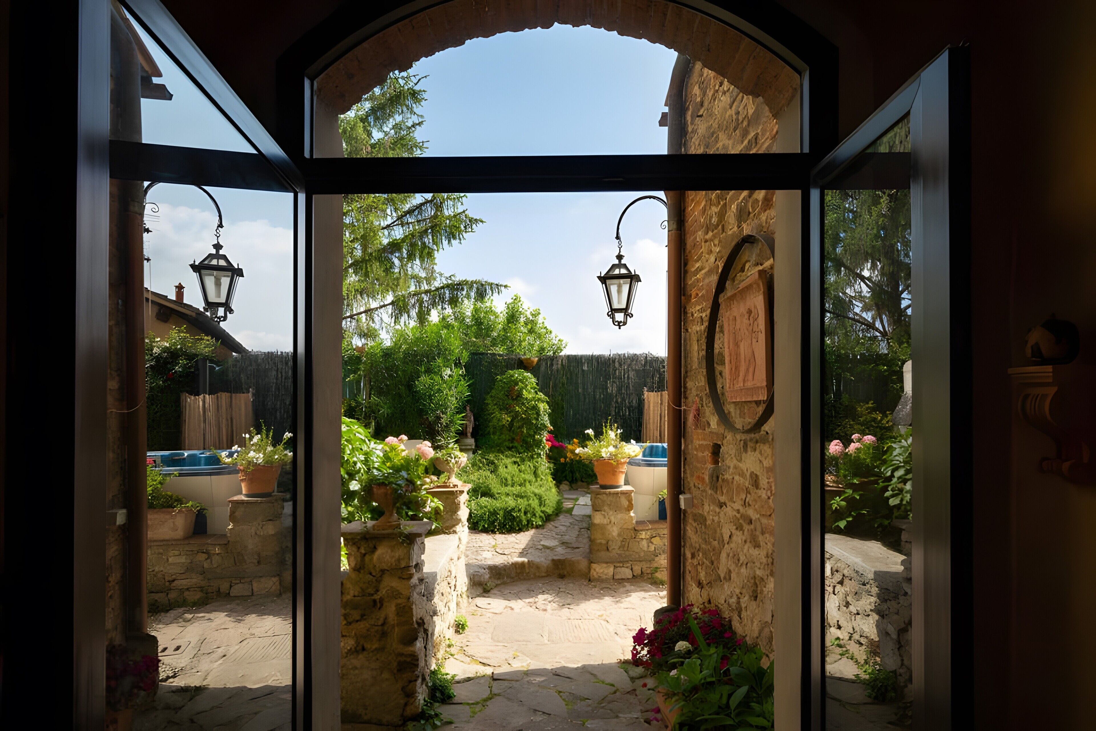 Un arco d'ingresso conduce a un sentiero in pietra, circondato da piante in vaso e un giardino curato.
