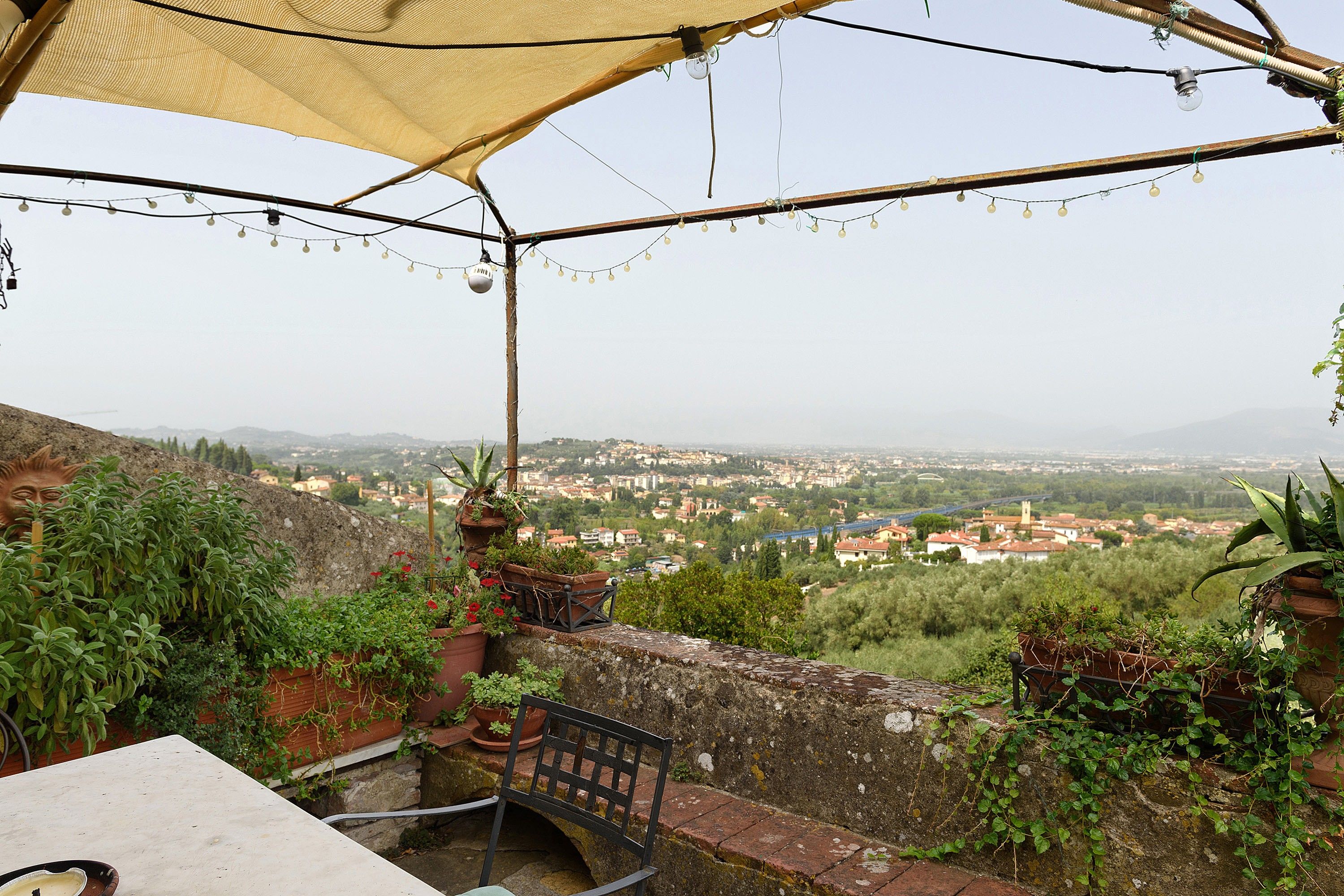 A terrace with a view of a town, potted plants, and a bench.