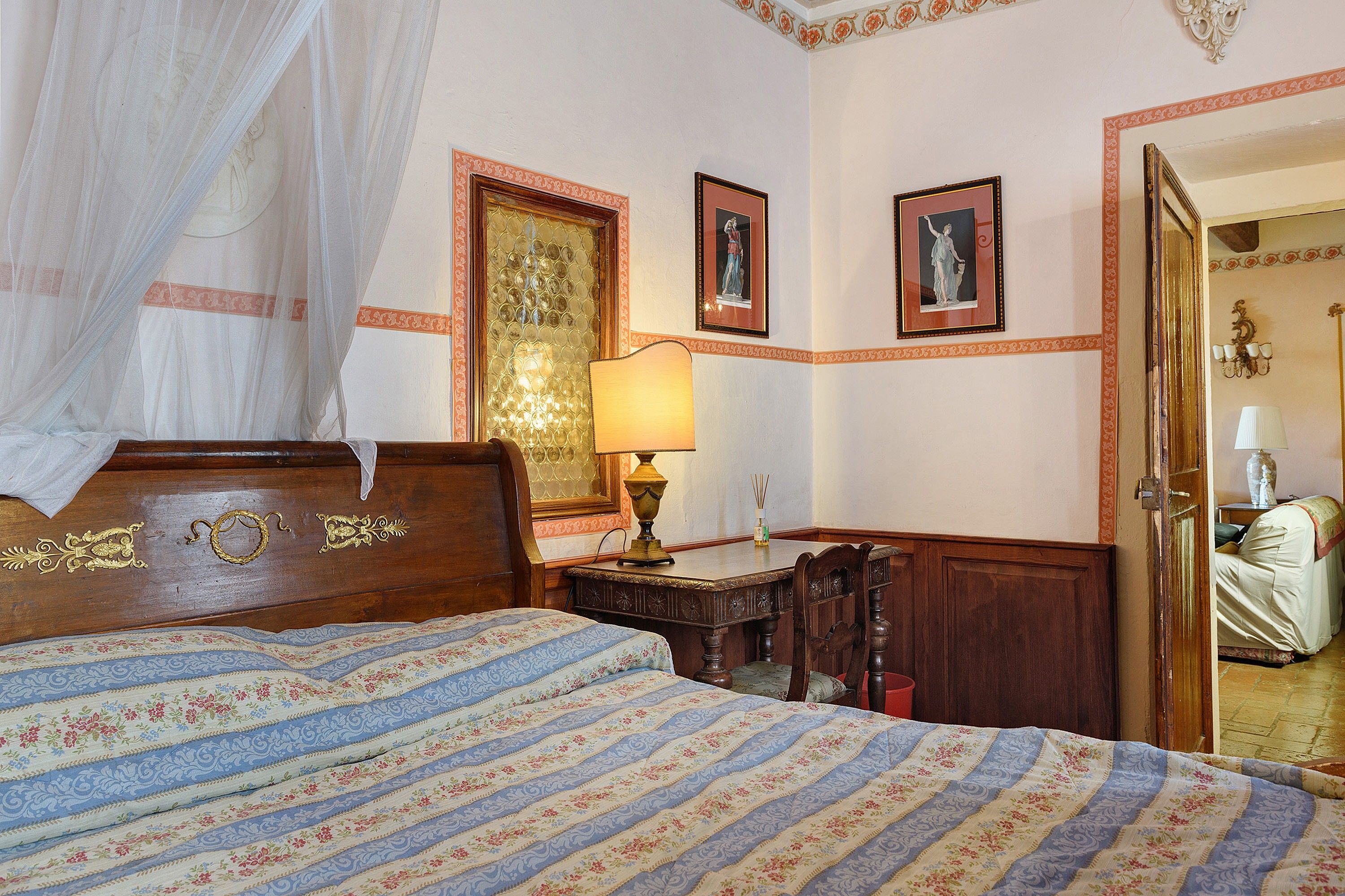 Una camera da letto con un letto, un comodino, una lampada e una porta che dà su un'altra stanza.