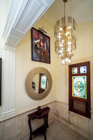 Een kamer met een grote spiegel, een lijstwerk schilderij, een kroonluchter en een glas-in-lood raam.