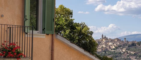A building with a balcony, green shutters, and a view of a distant town.