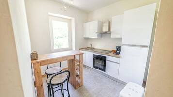 Eine kompakte Küche mit Holztisch und zwei Stühlen, einem eingebauten Backofen und weißen Schränken.