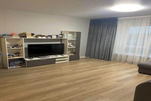 A living room with a flat-screen TV, wooden flooring, a sofa, and a bookshelf.