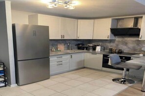 A modern kitchen with white cabinets, a stainless steel refrigerator, a sink, and a bar stool.