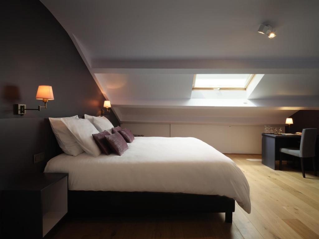 Un dormitorio con cama, mesitas de noche, un escritorio y un tragaluz.