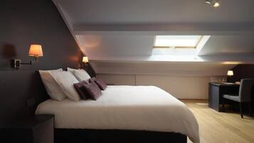 Un dormitorio con cama, mesitas de noche, un escritorio y un tragaluz.