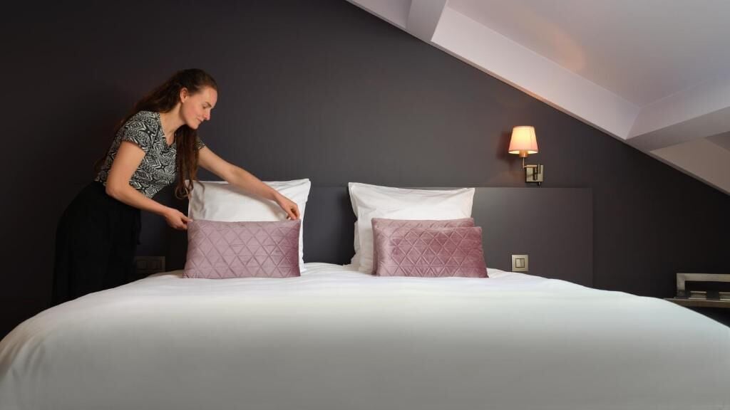 Ein Hotelzimmer mit Bett, Kissen, einem Nachttisch und einer Wandlampe.