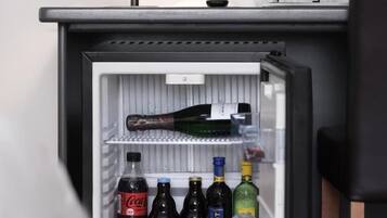 Un frigorifero con una bottiglia di Coca-Cola, diverse bottiglie di vino e due bottiglie trasparenti sullo scaffale superiore.