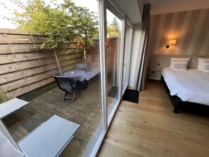 A hotel room with a sliding glass door leading to a patio area, a bed, a bedside table, and a small seating area with a table and chairs. - Hôtel Le 24 (Spa)