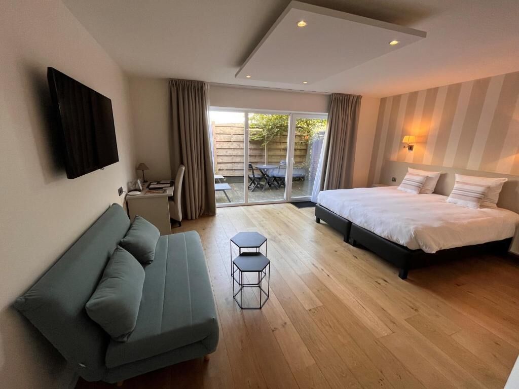 Un dormitorio con cama, sofá, una mesita y televisor.