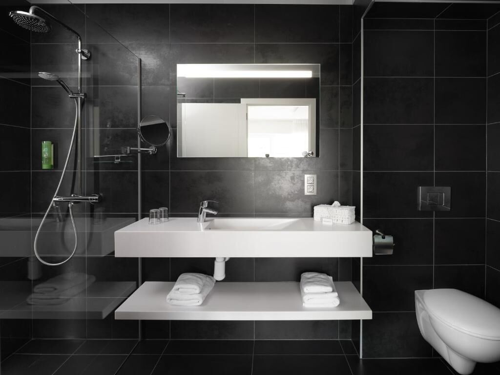 Une salle de bain moderne avec un grand miroir, un lavabo blanc, une douche et des toilettes.