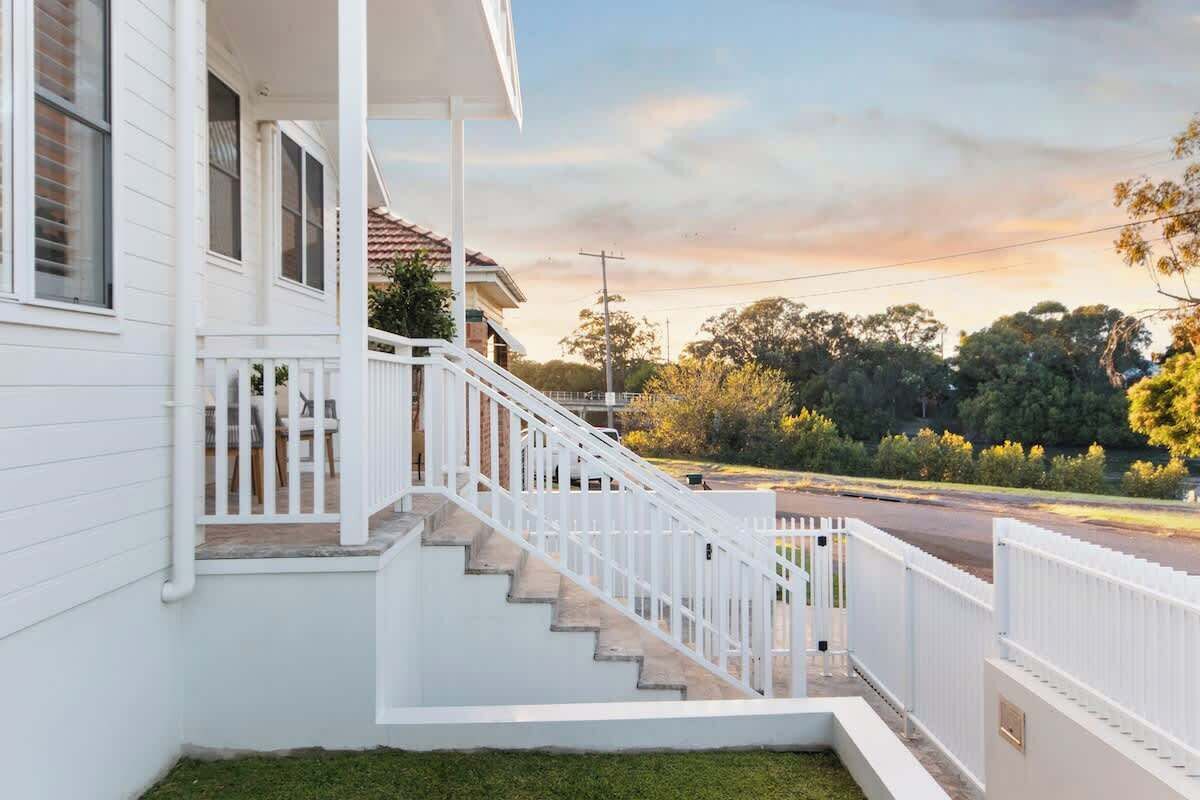 A white house with a front porch, a staircase, and a view of the street and trees.