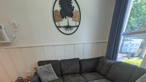 Um sofá modular com um tapete cinzento, uma mesinha de madeira e um enfeite de árvore fixado na parede.