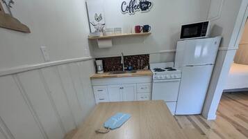 A compact kitchen with a wooden table, white cabinets, a microwave, and a coffee-themed wall decoration.