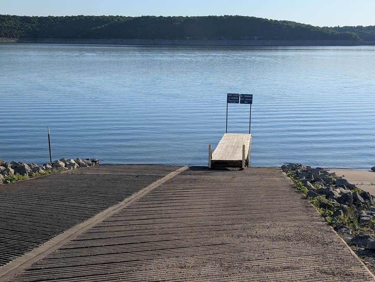 Une jetée en bois mène à un lac paisible, et un panneau indique la présence d’un espace de stationnement.