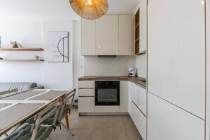 Une cuisine compacte dotée d’un four encastré, d’un plan de travail en bois et de meubles de rangement blancs.