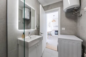 Un baño moderno con mampara de vidrio, lavamanos blanco y zona de ducha.