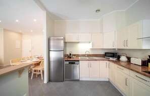 Eine moderne Küche mit einem Edelstahlkühlschrank, einer Spülmaschine, einer Mikrowelle und einem Toaster. Es gibt einen Essbereich mit einem Tisch und Stühlen.