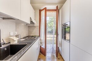 Una cocina estrecha con estufa a gas, lavamanos y horno empotrado.