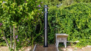 Een tuin met een hoge, zwarte metalen constructie, een stenen bank en weelderige groene beplanting.