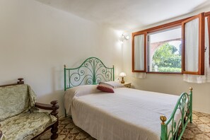 Un dormitorio con una cama individual, una mesita de noche, una lámpara, una silla y una ventana con cortinas.
