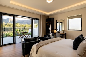 Habitación de hotel con una cama grande, un escritorio, una silla y un balcón con vistas a las montañas.