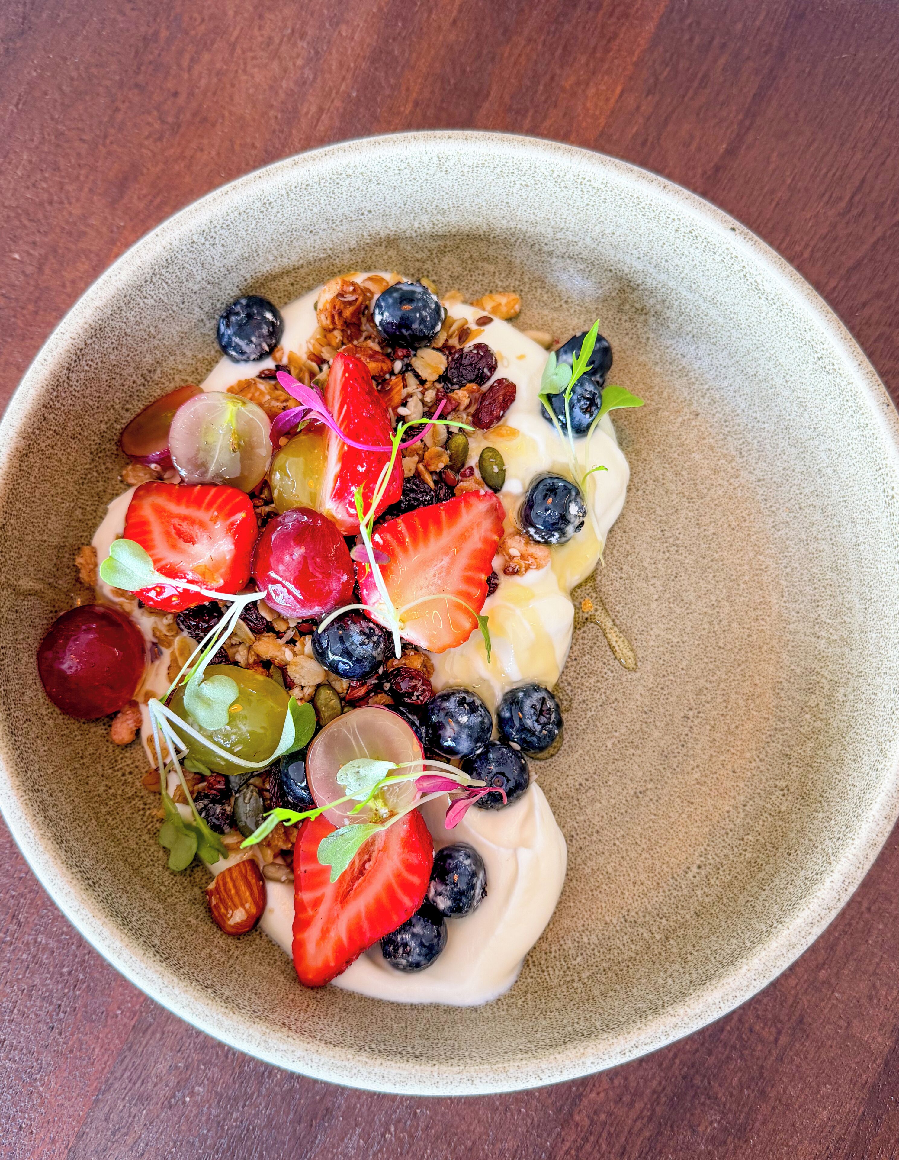 Un tazón de yogur cubierto de frutas, granola y semillas.