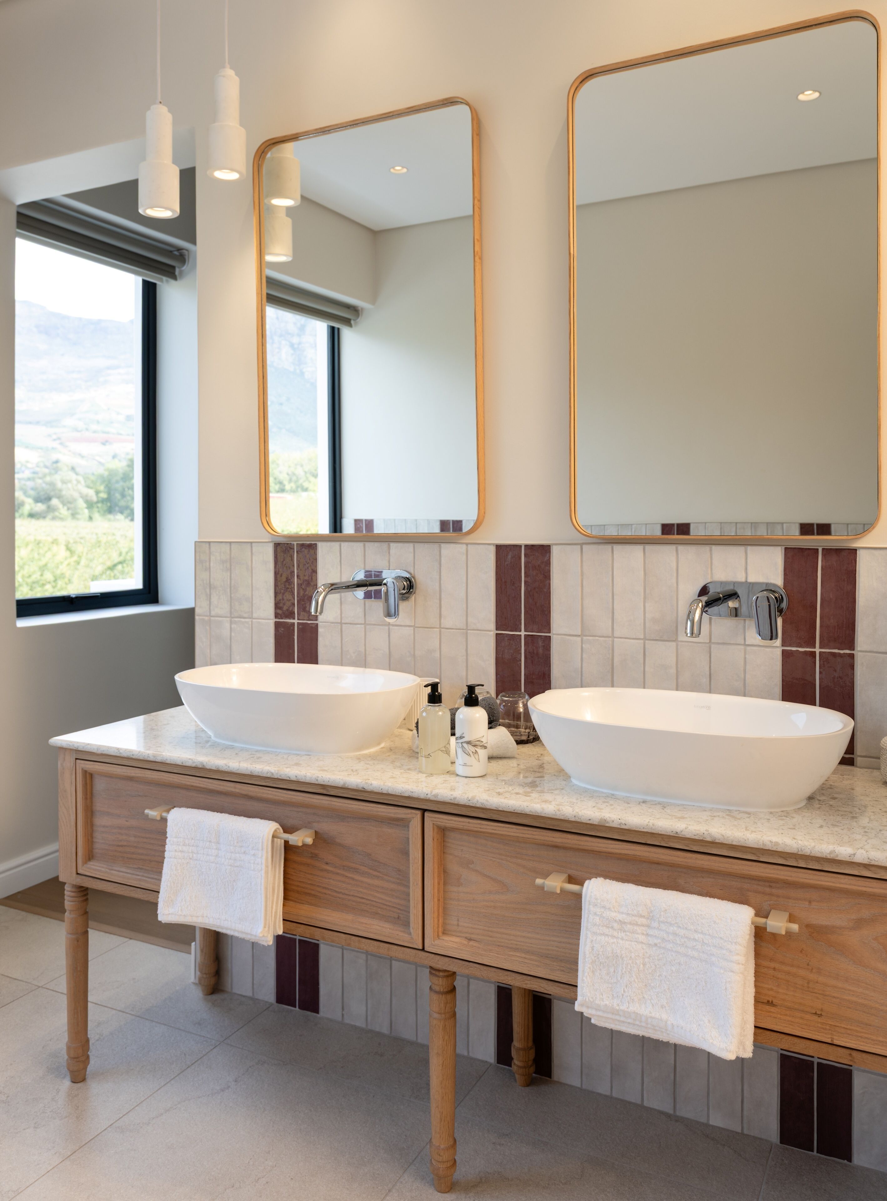 Un baño moderno con dos lavamanos tipo sobremesa, tocador de madera y un espejo grande.