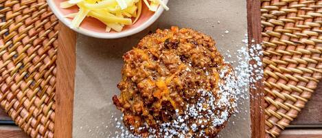 A wooden board with a baked item, shredded cheese, and a small bowl of butter on a woven mat.