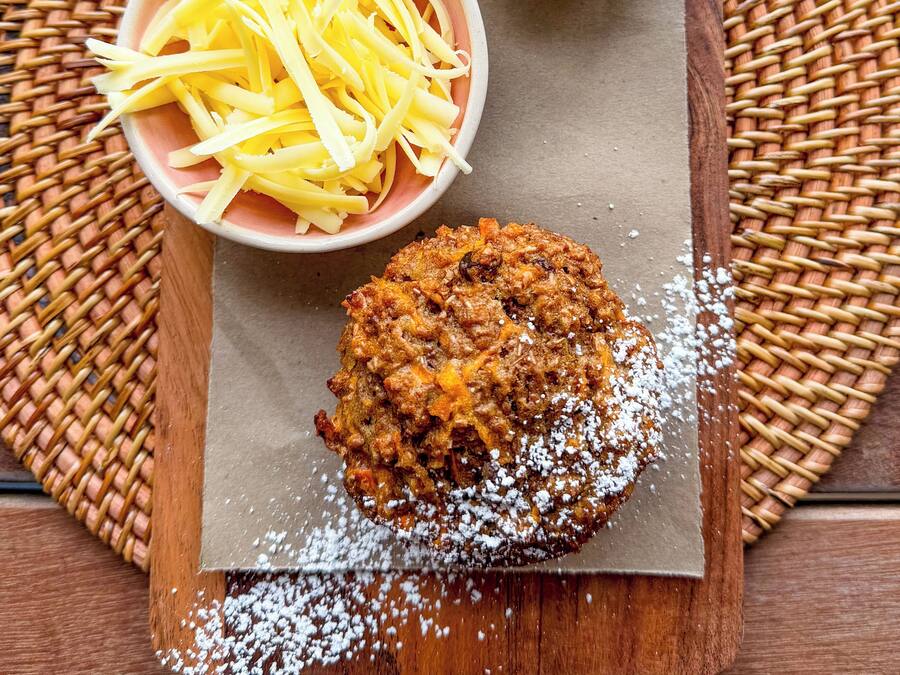 A wooden board with a baked item, shredded cheese, and a small bowl of butter on a woven mat.