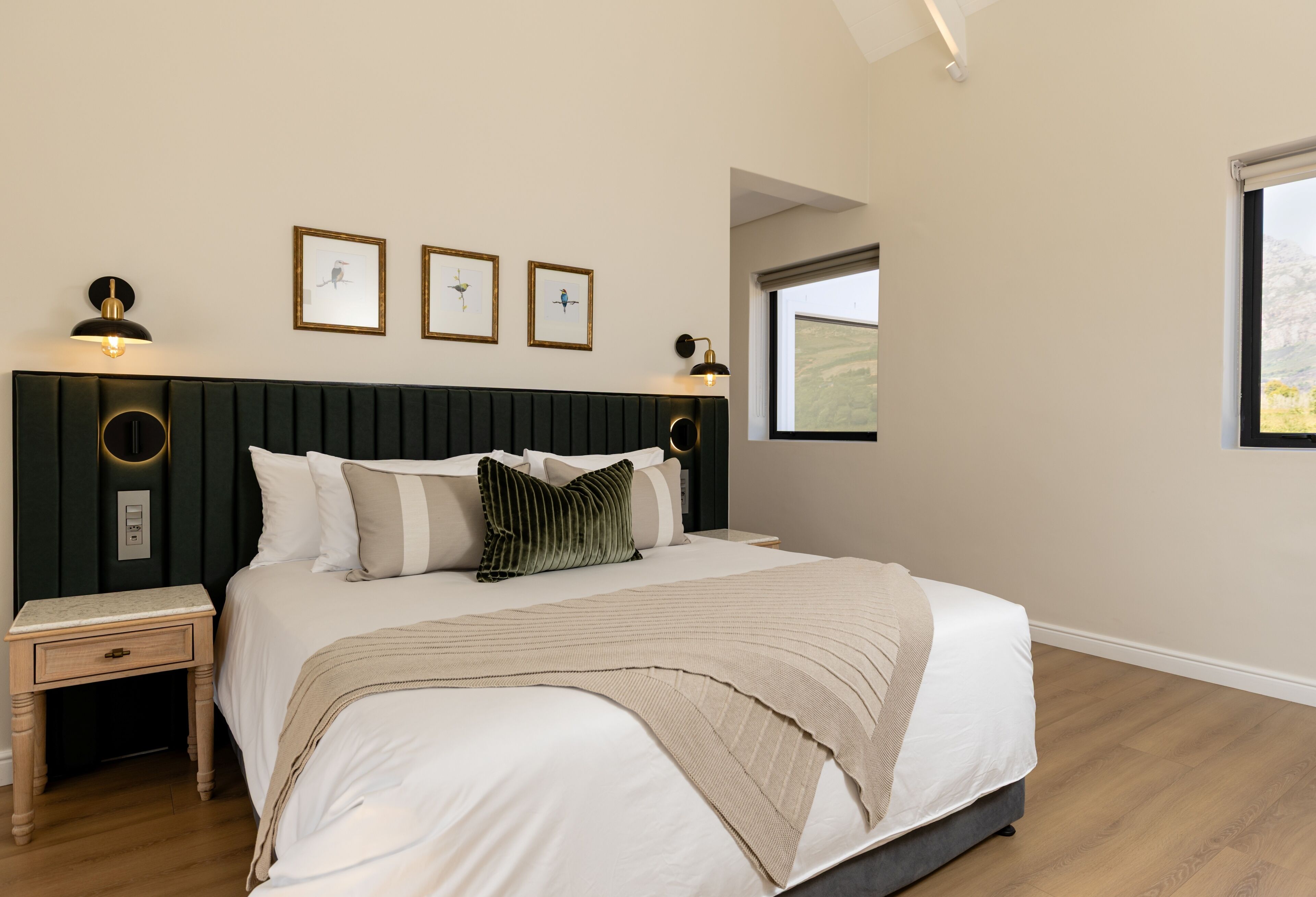 A bedroom with a bed, bedside tables, a nightstand, a window, and wall-mounted artwork.
