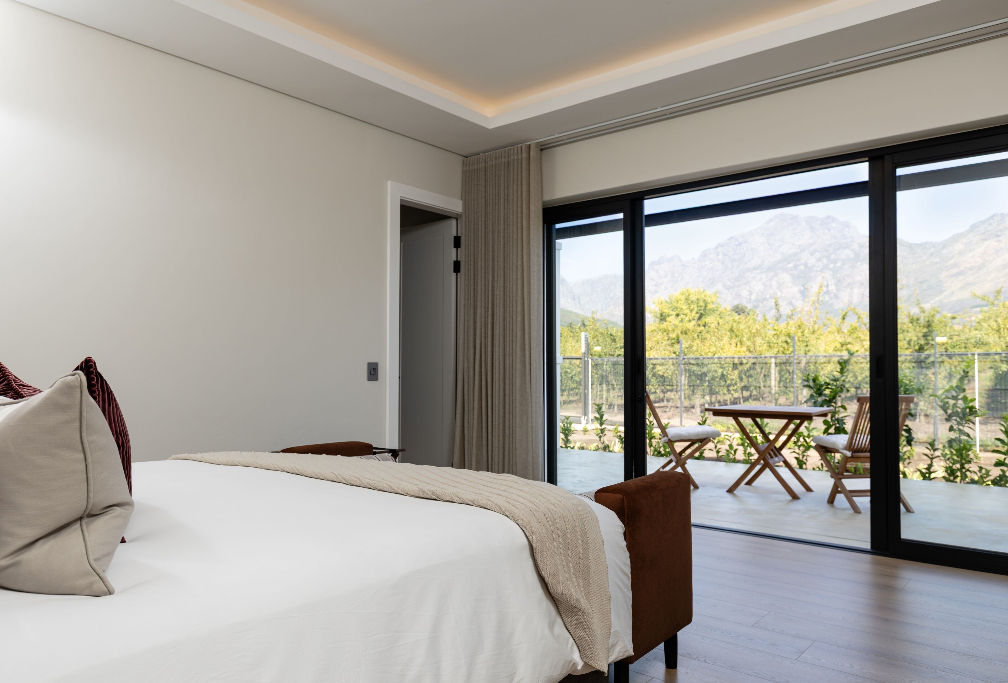 Een slaapkamer met een groot bed, uitzicht op een balkon met tuinmeubilair en een berg op de achtergrond.