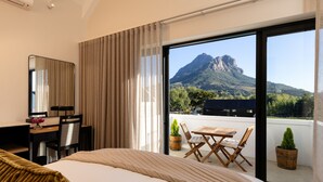 Een hotelkamer met een bed, een bureau, een stoel, een balkon met een tafel en stoelen, en uitzicht op de bergen.