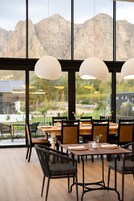 Un restaurante con una amplia ventana que ofrece vistas a las montañas, mesas de madera y sillas negras.