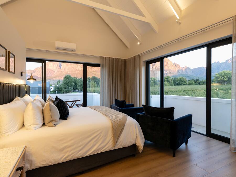 A modern hotel room with a large bed, a desk, and a view of mountains through the windows.