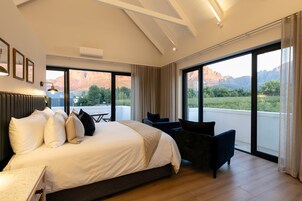 Habitación de hotel moderna con una cama grande, un escritorio y vistas a montañas desde las ventanas.