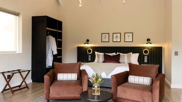 Un dormitorio con una cama, dos sillones, una mesita, un armario e iluminación en la pared.