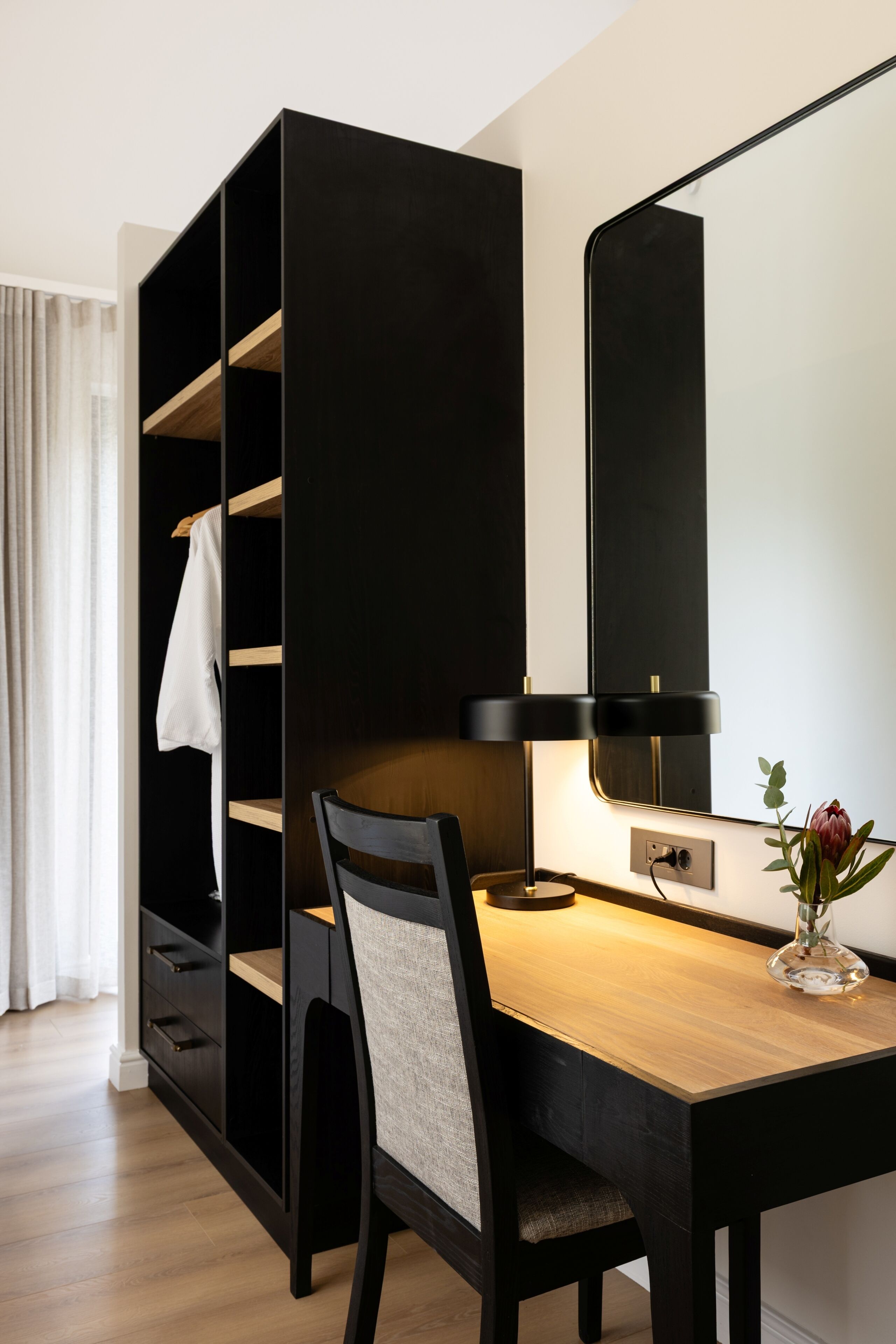 Ein modernes Zimmer mit einem Holztisch, einem schwarzen Stuhl, einer schwarzen Regaleinheit und einem wandmontierten Spiegel.