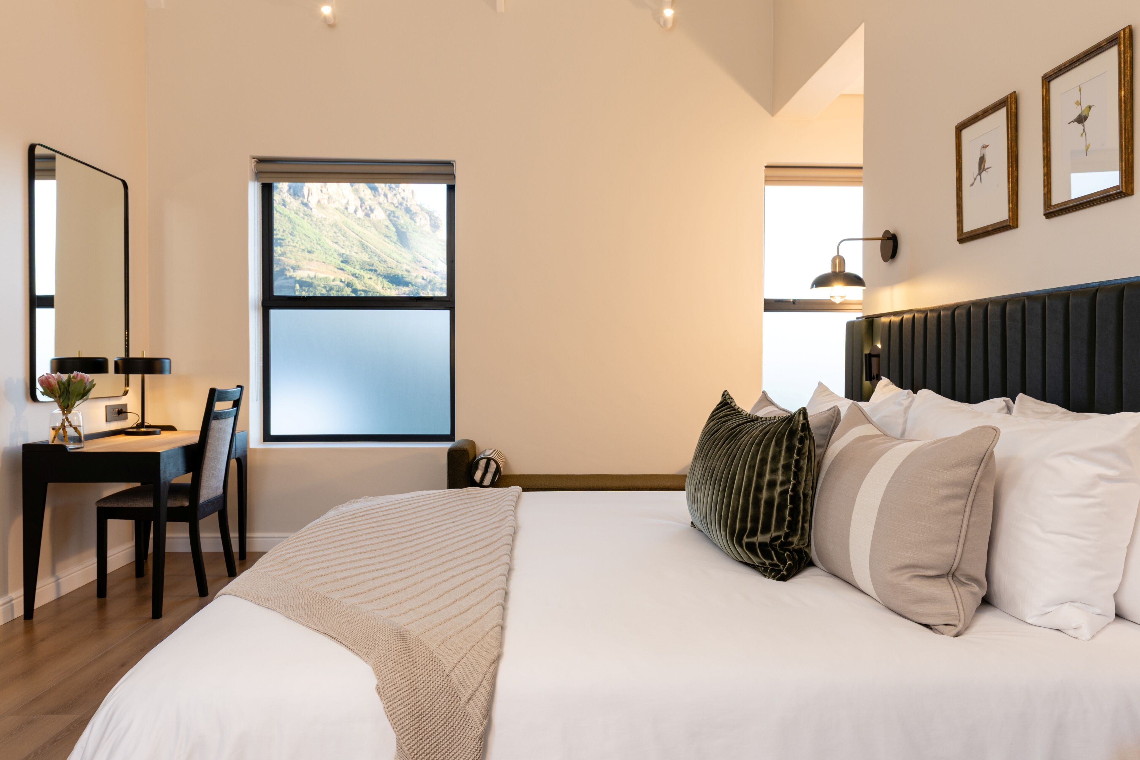 Un dormitorio con cama, escritorio y silla. Se ve una ventana con vistas a la montaña.