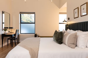 Un dormitorio con cama, escritorio y silla. Se ve una ventana con vistas a la montaña.