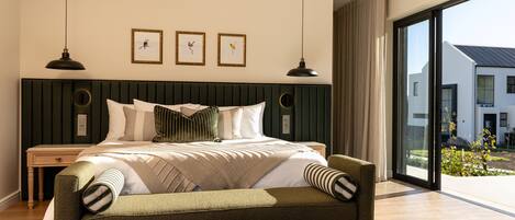 A modern bedroom with a large bed, a green upholstered sofa, a round side table, and a view of the outside.